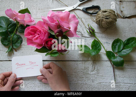 Blick von oben auf die weiblichen Dekorateur Holding "Danke"-Karte, die die Rosen auf dem Holztisch, Konzepte - fiorist, Beruf, Hobby, Small Business Stockfoto