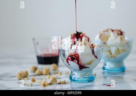 Vanilleeis in blauer Schüssel, auf weißem Hintergrund, Seitenansicht, Nüsse und Beeren Sirup über Eis. Stockfoto