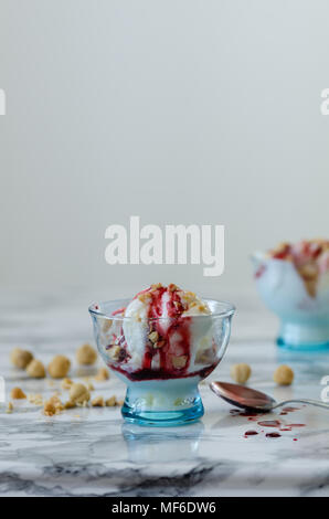 Vanilleeis in blauer Schüssel, auf weißem Hintergrund, Ansicht von oben, Nüsse und Beeren Sirup über Eis. Stockfoto