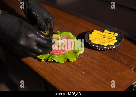 Frau in Schwarz Küchenchef bereitet ein Burger in einem Restaurant Stockfoto