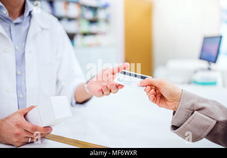 Nicht erkennbare Kunden eine Kreditkarte zu einem männlichen Apotheker. Stockfoto