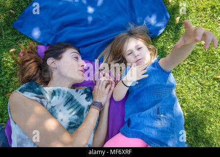 Vier Jahre alt blond Kind spielen mit Hand, liegend mit Frau Mutter auf Handtücher in das grüne Gras der Park Stockfoto