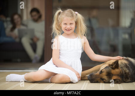 Lächelnde Mädchen spielen mit Hund ausserhalb des Hauses mit Blick auf die Kamera Stockfoto