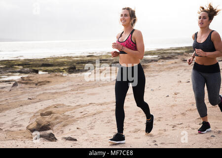 Junge Mädchen joggen am Meer in dunklen Strumpfhosen und modernen Pflanzenschutz tops Suche happy Stockfoto