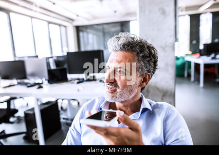 Portrait von Reifen Geschäftsmann mit Smartphone im Büro Stockfoto