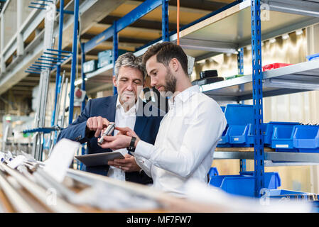 Unternehmer während der Sitzung mit Tablet und Produkt in der Produktionshalle Stockfoto
