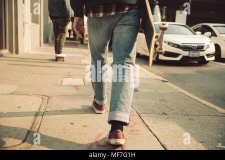 Niedrige Abschnitt des Menschen zu Fuß auf Gehweg mit Skateboard Stockfoto
