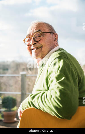 Portrait von lächelnden älteren Mann sitzt auf Stuhl am Fenster Stockfoto