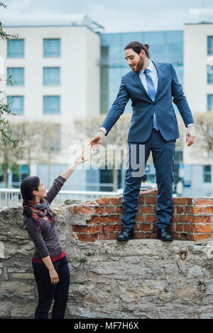 Unternehmer stehen auf einer Wand erreichen seine Hand für Frau Stockfoto