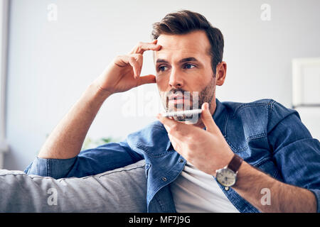 Sorgen Mann sitzt auf einem Sofa mit Handy Stockfoto