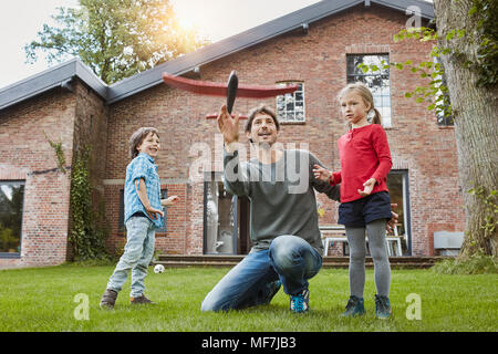 Vater mit zwei Kindern das Spielen mit Spielzeug Flugzeug im Garten ihres Hauses Stockfoto