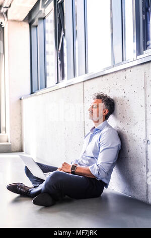 Reifen Geschäftsmann mit Laptop sitzen auf dem Boden an die Wand gelehnt Stockfoto