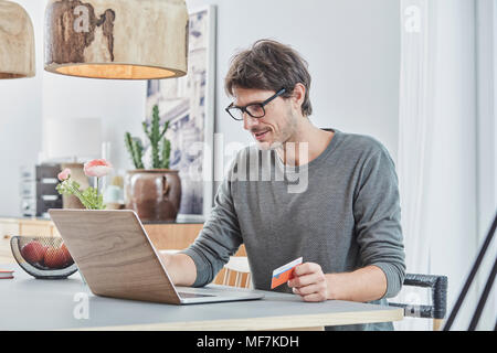 Mann hält eine Karte mit Laptop auf dem Tisch zu Hause Stockfoto