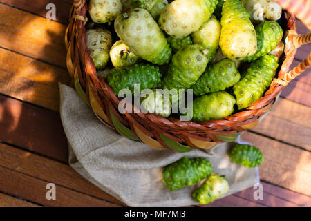 Warenkorb Noni und Noni auf braunem Tuch auf Holztisch mit Natur Hintergrund, Ansicht von oben. Stockfoto