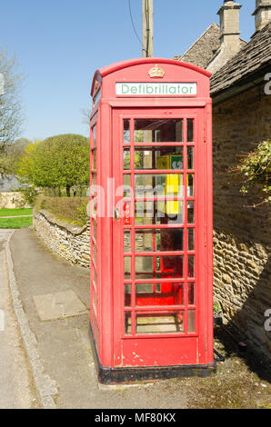 Alte rote Telefonzelle mit einem Defibrillator im hübschen Dorf Cotswold Upper Slaughter in Gloucestershire, Vereinigtes Königreich ausgestattet Stockfoto