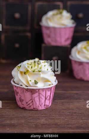 Hausgemachte Schokolade Muffins oder Cupcakes mit Vanillecreme und Pistazien auf dem hölzernen Hintergrund, getönt Stockfoto