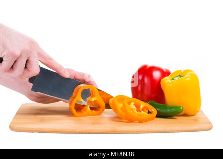 Eine orange Paprika in Scheiben auf einem Bambus Schneidebrett schneiden. Andere farbige Paprika sind in der Nähe. Stockfoto