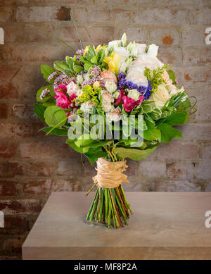 Schönen Blumenstrauß, bunte Rosen mit grünen Blättern steht auf einem Tisch in der Nähe der Wand Stockfoto