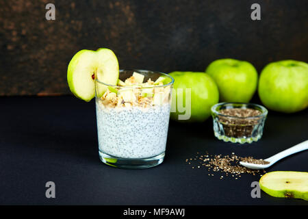 Gesunde chia Blutwurst mit Äpfeln und Müsli in Glas auf schwarzem Hintergrund. Vegan cremige Frühstück. Detox und gesunden superfoods Frühstück Konzept. Stockfoto