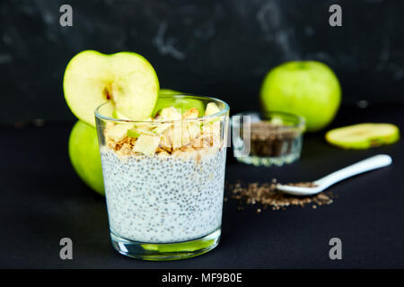 Gesunde chia Blutwurst mit Äpfeln und Müsli in Glas auf schwarzem Hintergrund. Vegan cremige Frühstück. Detox und gesunden superfoods Frühstück Konzept. Stockfoto