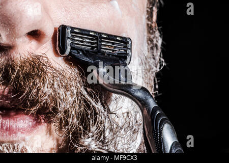 Mann in Rasierschaum rasiert seinen Bart und Schnurrbart mit einem Rasiermesser, Foto close-up Stockfoto