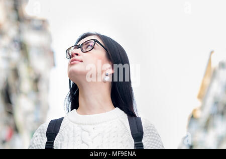 Attraktive junge Single brunette Mädchen Touristen zu Fuß die Straße runter. Reflexion der Lichter der Stadt in Ihrer Brille. Verschwommenes Gebäude im Hintergrund. Stockfoto