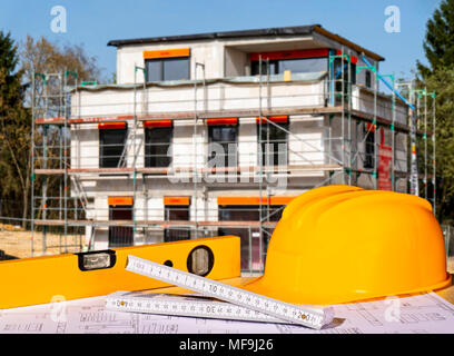 Helm, Wasserwaage, Zollstock und Baupläne mit einer Shell im Hintergrund Stockfoto