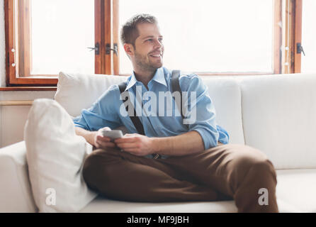 Stattliche Mann sitzt auf einem Sofa und texting von seinem smart phone Stockfoto