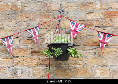 Eine Zeichenkette von Union Jack Wimpelketten hing an einem Garten Wand mit einem hängenden Korb Stockfoto