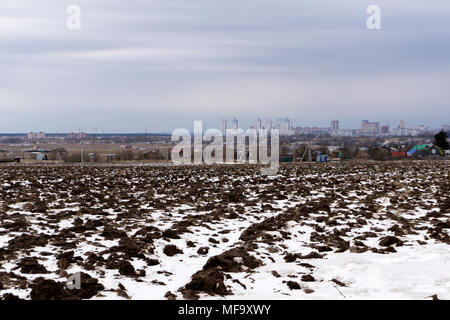 Feld mit der Schneeschmelze im Frühjahr gepflügt, mit einem Dorf in der Ferne und eine Stadt am Horizont Stockfoto