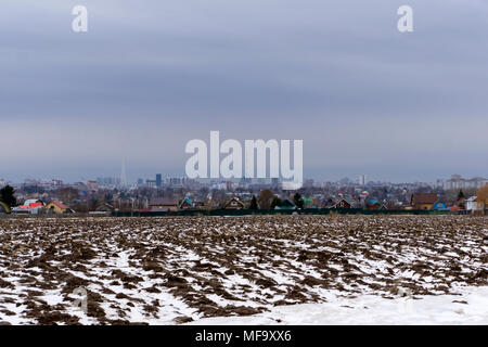 Feld mit der Schneeschmelze im Frühjahr gepflügt, mit einem Dorf in der Ferne und eine Stadt am Horizont Stockfoto