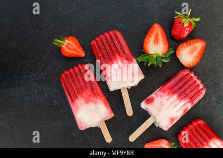 Hausgemachte Vegan Erdbeere Popsicle mit Erdbeersaft und Kokosmilch auf dunklem Marmor Hintergrund. Sommer essen Konzept. Ansicht von oben. Stockfoto