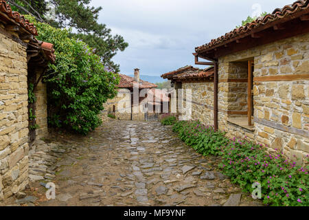 Knysna, Bulgarien - engen, gepflasterten Straßen und rustikalen traditionelle Häuser aus Stein und Holz mit bigroot cranesbill (Geranium macrorrhizum) zusammen. Stockfoto