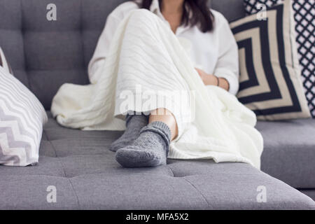 Junge Frau sitzt auf einem Sofa in der Decke abgedeckt, konzentrieren Sie sich auf Ihre grauen Socken Stockfoto