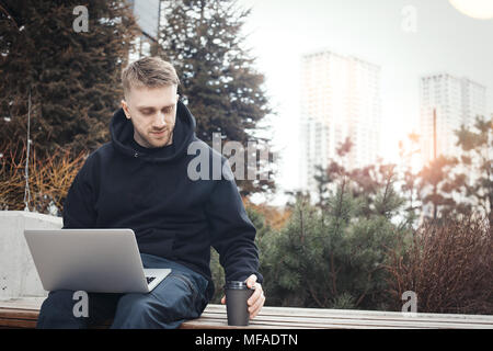 Junger Mann mit Laptop auf den Knien. Schwarz Kaffee Tasse ist neben ihm. Stockfoto