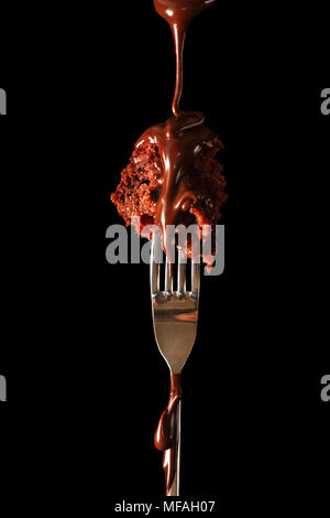 Geschmolzene Schokolade giessen auf ein Stück muffin auf eine Gabel, mit einem Flash und eine silberne Reflektor fotografiert. Stockfoto