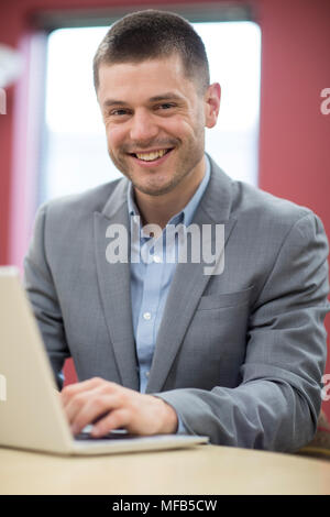 Portrait von Geschäftsmann am Schreibtisch im Büro mit Laptop Stockfoto