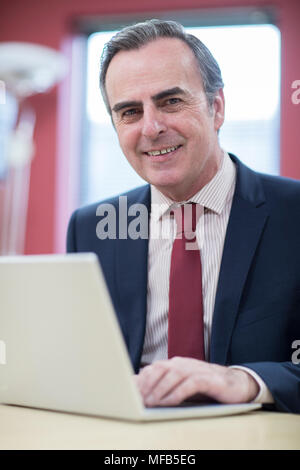 Portrait von Reifen Unternehmer Sitzen am Schreibtisch im Büro mit Laptop Stockfoto