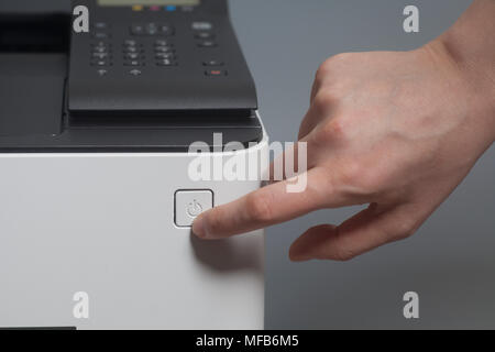 Woman's Hand Druck auf den Knopf an der Farblaserdrucker auf Grau Stockfoto