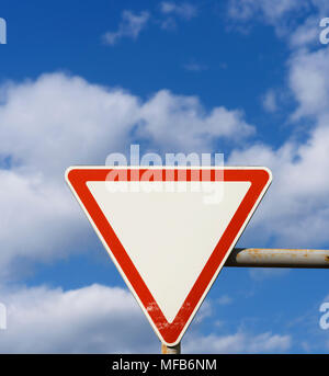 Schild der Priorität, für die ein Treiber weg zu Fahrzeugen, die entlang einer überquert Straße gegen einen blauen Himmel mit Wolken zu geben Stockfoto