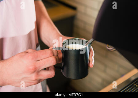 Hände, die Tasse mit Milch für den Kaffee mit Maschine. Barista mit Krug, Milchschaum. Stockfoto