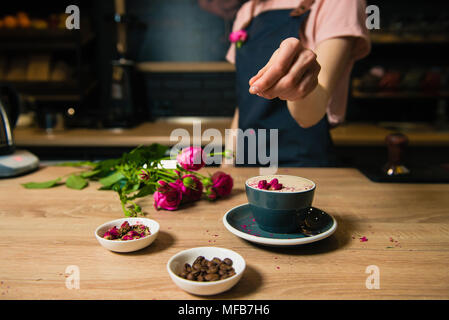 Prozess der Kaffee trinken mit Rosenknospen und Bohnen auf den Tisch. Junge Barista, Rose raf Kaffee. Stockfoto