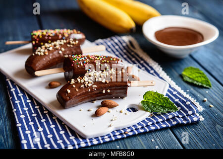 Frische Bananen, umhüllt mit Schokolade und sprengte mit gehackten Mandeln und bunten Streuseln Stockfoto