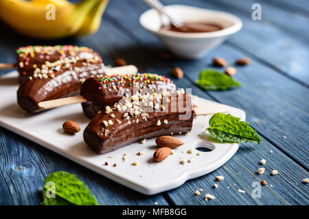 Frische Bananen, umhüllt mit Schokolade und sprengte mit gehackten Mandeln und bunten Streuseln Stockfoto