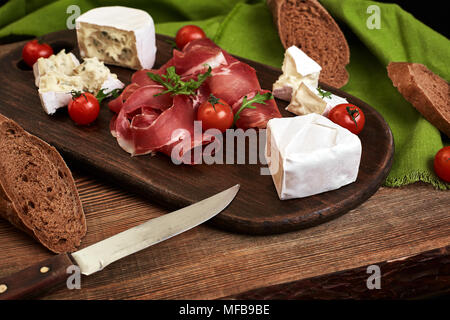 Käse, Schinken, Brot, Gemüse und Gewürzen auf Holzbrett auf schwarzen Hintergrund mit Kopie Raum Stockfoto