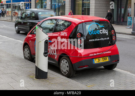 Eine kleine rote Umweltfreundliche elektrisch angetriebene Auto zu einer Ladestation im Zentrum der Hauptstadt von London angebracht. Autos der Zukunft Stockfoto