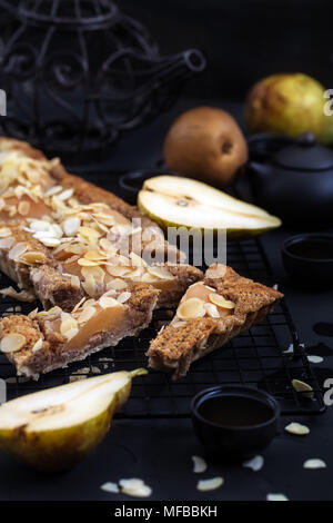 Frangipane Tarte mit pochierten Birnen und Mandel Blütenblätter. Low Key. Stockfoto