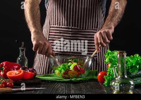 Mann Zubereitung Salat mit frischem Gemüse auf einem Holztisch. Kochen leckere und gesunde Lebensmittel Stockfoto