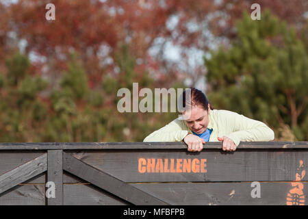 Eine junge Frau, die Kämpfe um eine Holzwand Hindernis am schlammigen Brute Challenge Rennen, am 21. November 2015 Aufstieg in Buford, GA. Stockfoto