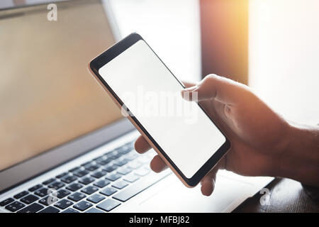 Junger Mann mit Tattoo holding Handy in der rechten Hand und Arbeiten am Laptop Stockfoto